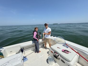 A young angler and an adult are fishing together on a boat, with the child holding a fishing rod and smiling, showcasing a fun day on the water.