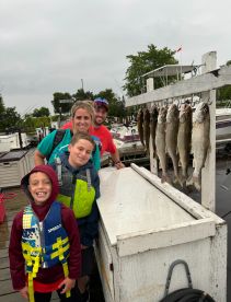 A family poses proudly in front of their catch of Walleye displayed on a board at the dock, showcasing a fun day of fishing.