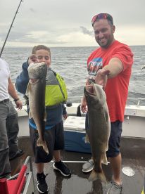 A young angler and an adult proudly displaying their catch of Lake Trout while fishing on a boat, showcasing a fun family fishing experience.