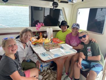 A family enjoying a meal inside a fishing boat, showcasing a cozy atmosphere with snacks and drinks, perfect for a day out on the water.