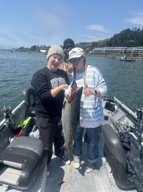 Two young anglers proudly displaying a large fish on a boat during a fishing trip, with a scenic waterfront in the background.
