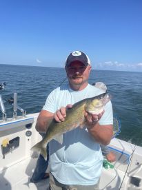 An angler proudly displaying a Walleye while fishing on a boat in open water.
