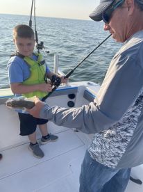 A young angler in a life jacket proudly holds a fish while fishing on a boat, showcasing a memorable moment on the water.
