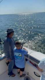A young angler and an adult are actively fishing on a boat, with the sun reflecting off the water, creating a vibrant fishing atmosphere.