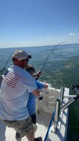 A young angler and an adult are working together to reel in a fish while fishing on a boat in open waters.