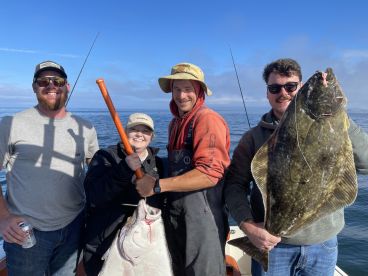 A group of four anglers proudly displaying their catch of a large Halibut while fishing on a boat in open waters.