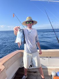Angler proudly displaying a large fish while fishing on a charter boat in clear blue waters.
