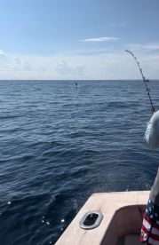 An angler is reeling in a fish while it jumps out of the water, showcasing the excitement of deep-sea fishing.
