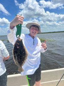 A young angler joyfully displaying a Flounder while fishing in a scenic waterway, showcasing a fun day on the water.