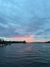 A scenic view of a calm waterway at sunset, showcasing the vibrant colors of the sky and a distant bridge.