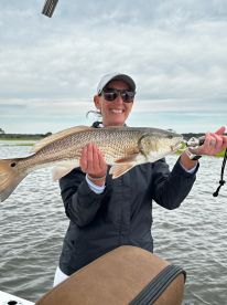 Angler proudly displaying a large Redfish while fishing on a calm waterway, showcasing a successful catch.