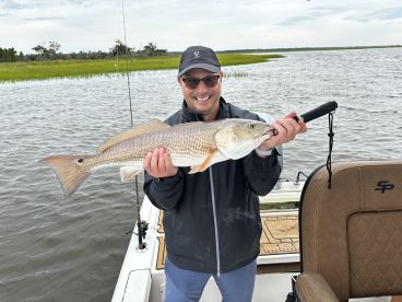 Angler proudly displaying a Redfish while fishing in a scenic coastal environment.