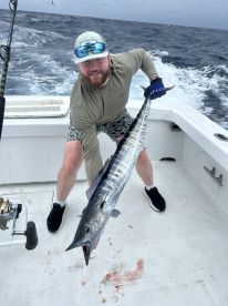 Angler proudly displaying a large Wahoo on a sportfishing boat, showcasing a successful deep-sea fishing trip.