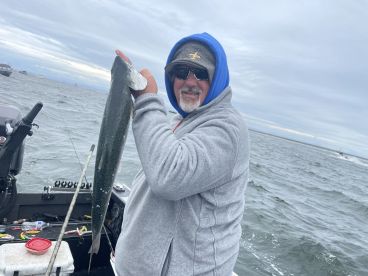 An angler proudly displaying a large fish while fishing on a boat in open water, showcasing a successful catch during a fishing trip.