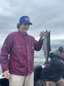 A young angler proudly displaying a freshly caught Salmon while fishing on a boat in a scenic coastal environment.