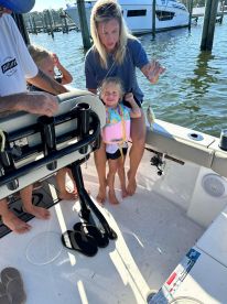 A young girl joyfully holds a small fish while sitting on a boat, accompanied by her mother and siblings, enjoying a family fishing trip.