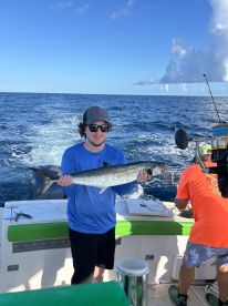 Angler proudly displaying a large Spanish Mackerel while fishing offshore, showcasing a vibrant blue sky and ocean backdrop.