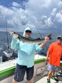 Angler displaying a large Barracuda while fishing offshore, with another fisherman in the background.