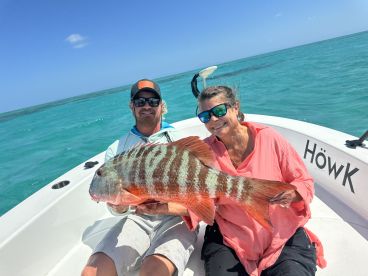 Two anglers proudly displaying a large Mutton Snapper while enjoying a sunny day on the water.
