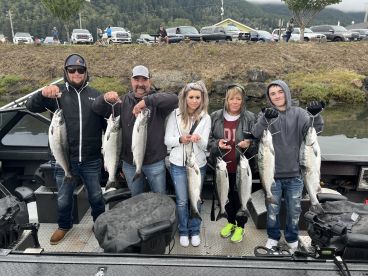 A group of anglers proudly displaying their catch of several Silver Salmon while aboard a fishing boat, showcasing a successful day on the water.