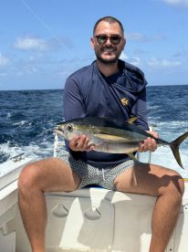 Angler proudly displaying a Yellowfin Tuna while seated on a boat in open waters, showcasing a successful offshore fishing trip.