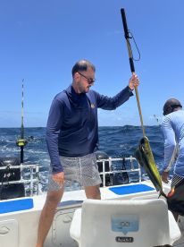 Angler reeling in a vibrant Mahi Mahi while fishing on a charter boat in open waters.