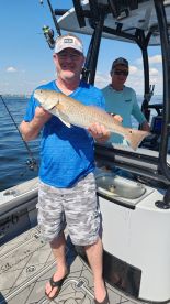 An angler proudly displaying a Redfish while fishing on a boat in a sunny coastal environment.