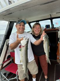 Two anglers proudly displaying their catch of Lake Trout aboard a fishing boat, enjoying a successful day on the water.