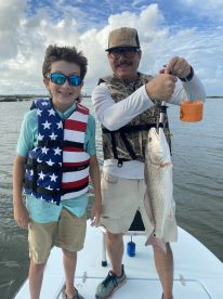 A young angler and an adult proudly displaying a Redfish while fishing in a scenic coastal environment.