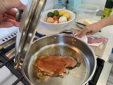 A cooking scene featuring a seasoned fish fillet in a pan, with ingredients and utensils visible in a kitchen setting.
