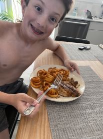 A young boy enjoying a meal of fish and curly fries at home, showcasing a casual dining moment.