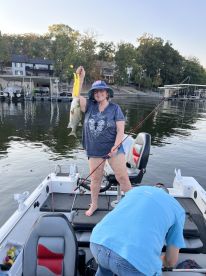 An adult angler proudly displaying a freshly caught striped bass while fishing from a boat on a serene lake.