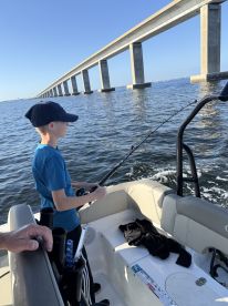 A young angler is focused on reeling in a catch while fishing near a bridge, showcasing the excitement of a day on the water.
