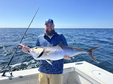 Angler proudly displaying a large Amberjack while fishing offshore, showcasing a beautiful day on the water.