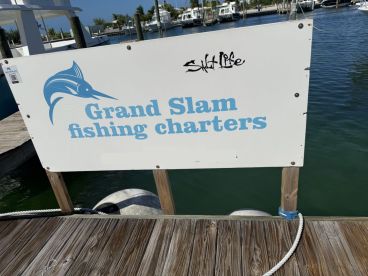 Signage for Grand Slam Fishing Charters displayed at a marina, featuring a marlin graphic and a scenic waterfront view.