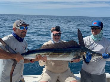 Three anglers proudly displaying a large Sailfish while out on the open ocean, showcasing their successful fishing trip.