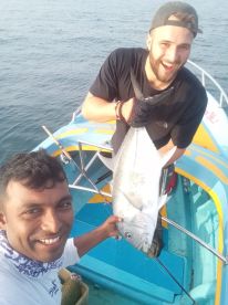Two anglers proudly displaying a large fish on a colorful boat during a fishing trip.
