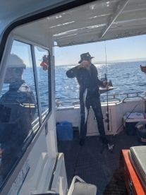 An angler reeling in a fish aboard a fishing boat, showcasing the excitement of the catch in a sunny marine environment.