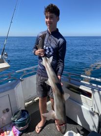 A young angler proudly displaying a large shark on a fishing boat, showcasing a successful day on the water.