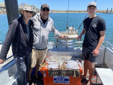 Three anglers posing on a boat with a cooler filled with freshly caught fish, showcasing a successful fishing trip.