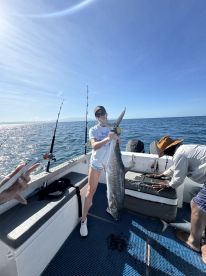 An angler proudly displaying a large King Mackerel while fishing on a charter boat in clear blue waters.