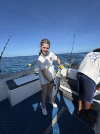 A young angler proudly displaying a large Barracuda while fishing on a boat in open waters.