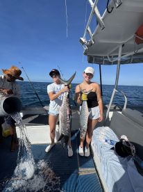 Two anglers proudly displaying their catch of large King Mackerel aboard a fishing charter in clear blue waters.