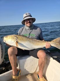 An angler proudly displaying a large Redfish while fishing from a small boat in open waters.