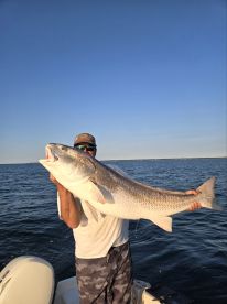 Angler proudly displaying a large Striped Bass while fishing on a boat in open waters.