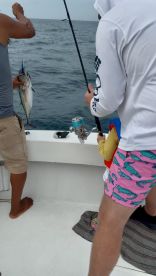 A young angler is actively reeling in a fish while an adult assists on a fishing charter in open waters.