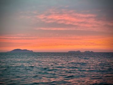 A serene sunset view over the ocean, featuring distant islands silhouetted against a colorful sky.