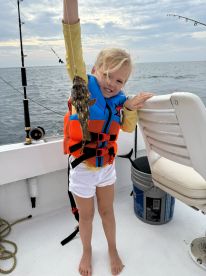 A young angler proudly displaying a caught fish while wearing a colorful life jacket on a fishing boat, showcasing a fun day on the water.