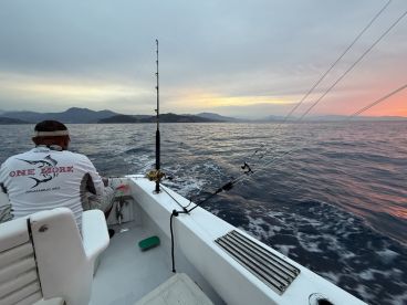 A lone angler seated on a fishing boat, preparing for a fishing session as the sun sets over the tranquil waters.