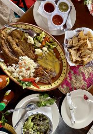 A vibrant display of a seafood meal featuring fried fish, rice, vegetables, and sauces, set on a colorful table.